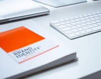 Ein minimalistischer Schreibtisch mit einem Buch über Markenidentität, einer weißen Tastatur und einem Laptop.