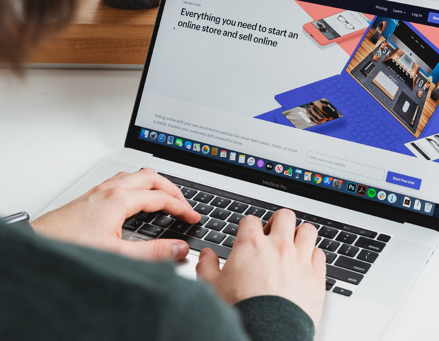Eine Person tippt auf einem MacBook Pro und arbeitet an einem Online-Shop, der auf dem Bildschirm geöffnet ist.