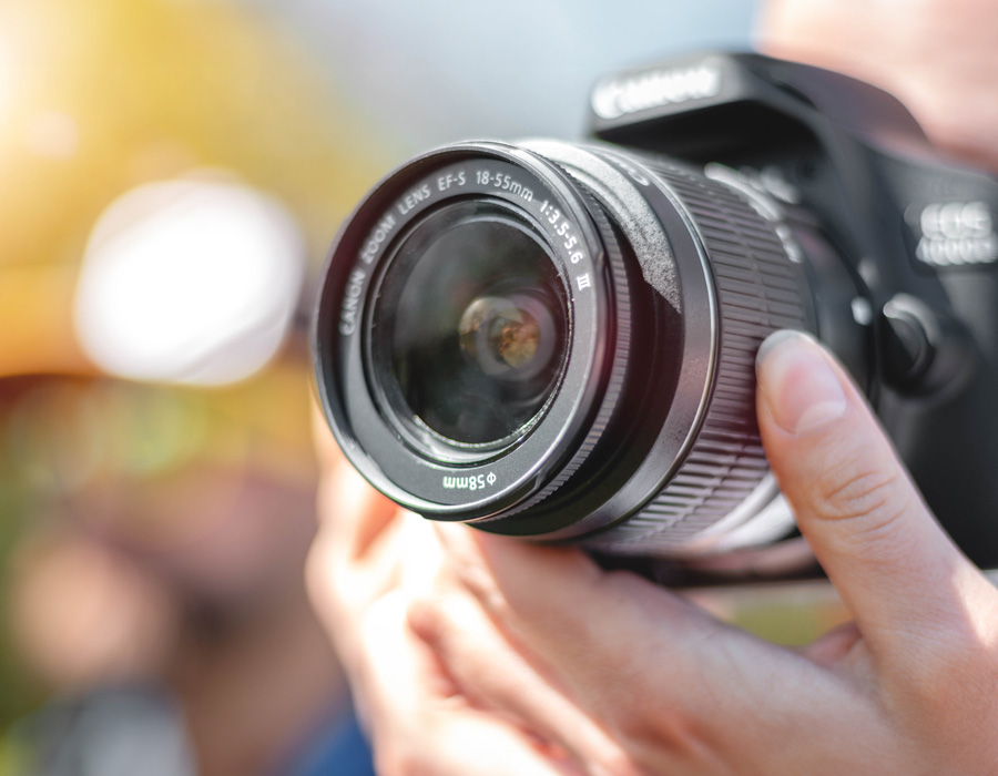 Eine Person hält eine Canon-Spiegelreflexkamera mit einem 18-55mm-Objektiv und fokussiert auf ein Motiv im Freien.